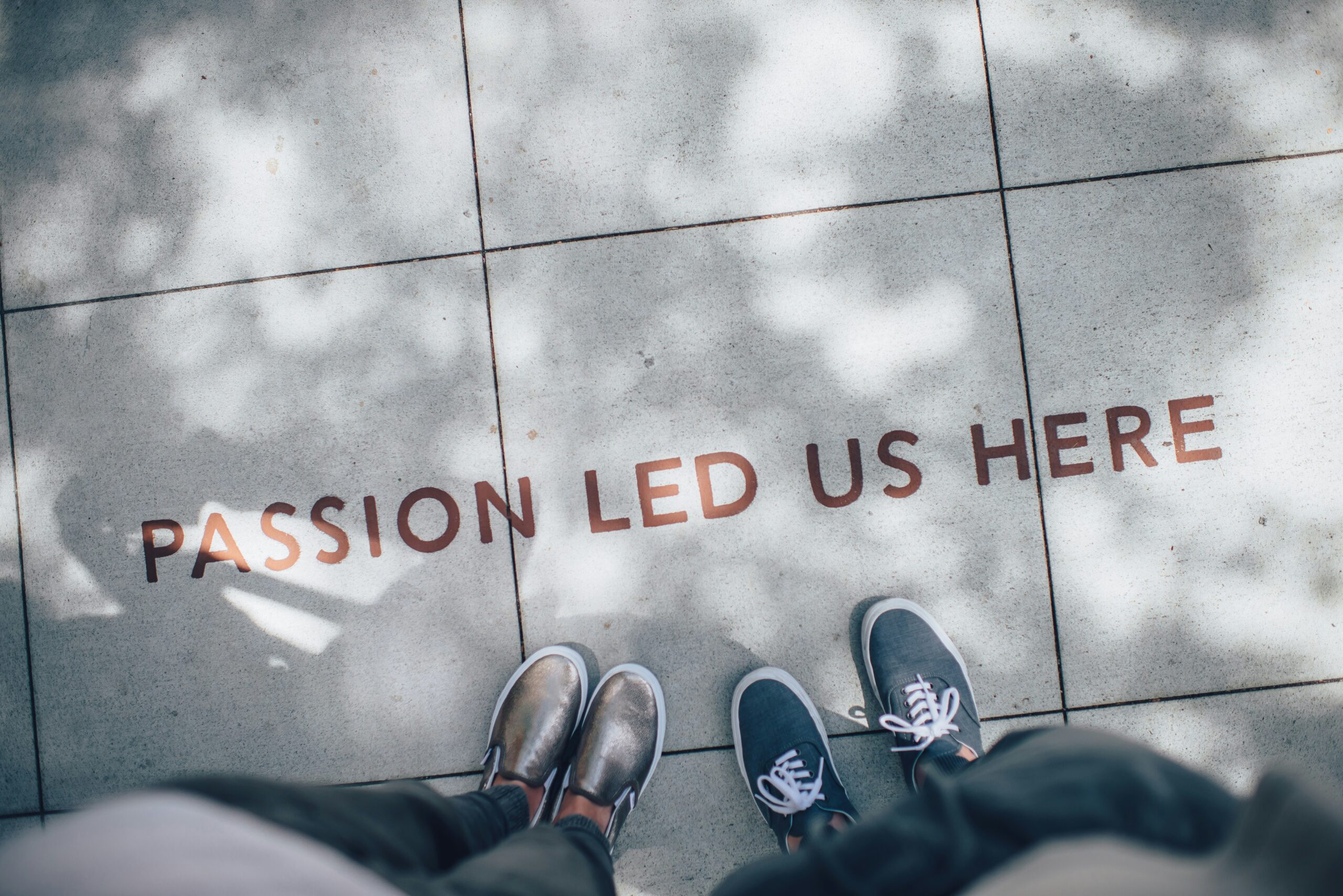 Photo of people's shoes and the concrete has the text written "Passion Led Us Here"