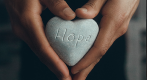Two hands holding a stone heart with the word hope written